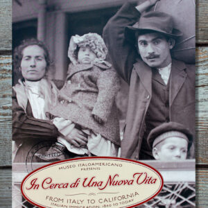 The exhibition catalogue In Cera di Una Nuova Vita, the cover featuring a black-and-white image of an Italian immigrant family of four disembarking from a boat. The exhibition title is in red on a light yellow oval background at the bottom of the cover.