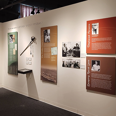 This wall is divided into four panels. The first panel on the far left, in green, has a title that is not readable. The second panel, in yellow, discusses traveling via sea. The last two panels, stacked one on top of the other, cover immigration laws and displaced people.