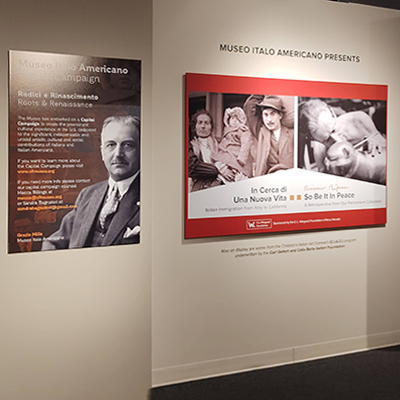 Title wall with a panel divided in two: on the left side, an image of a family of three immigrants descending from a ship; on the right side, a black and white image of Beniamino Bufano working on the cat sculpture. Adjacent to the title wall, in the column, there is a panel about the capital Capital campaign of the Museo with an image of A.P. Giannini.