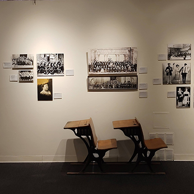 Below a mix of black and white images related to schools, there are a couple of school desks placed as objects.