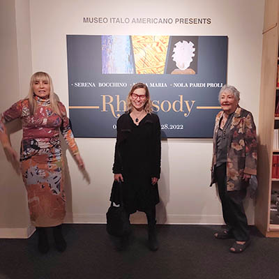 At the opening night, three artists stand in front of the title wall: Serena Bocchino on the left, Kara Maria in the center, and Nola Pardi Proll on the right.