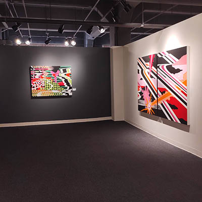 A corner where two walls meet, both adorned with abstract artworks by Kara Maria. The wall on the left is gray, and the wall on the right is white