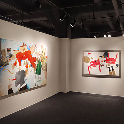 An image showing the corner of two walls. On the left wall, there is an artwork featuring a man dressed in red floating in the air, surrounded by other faces rendered in a less realistic style. There are also letters and bicycles. On the other wall, there is a mix of abstract elements, including legs from the bottom and details of a red table divided in half.