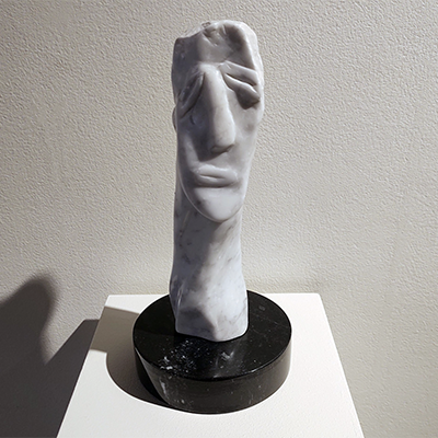 A marble sculpture by Nola representing a face. The face is depicted in a simple way with lines, and it is longer and narrower than a regular face. It is accompanied by a long neck