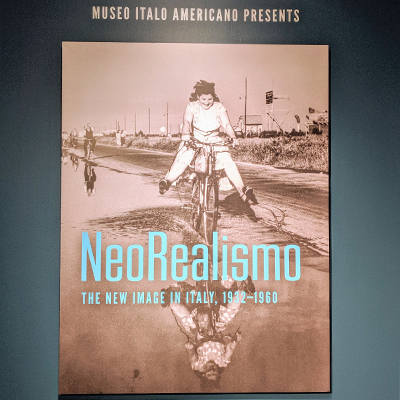 Poster of the Neorealismo exhibit. There is a black-and-white image of a girl riding a bicycle into a puddle and the text "Neorealismo: The New Image in Italy" in light blue.