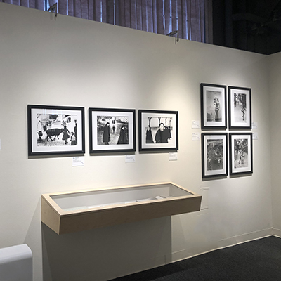 A white wall with seven black-and-white images and a display case hanging from the wall.