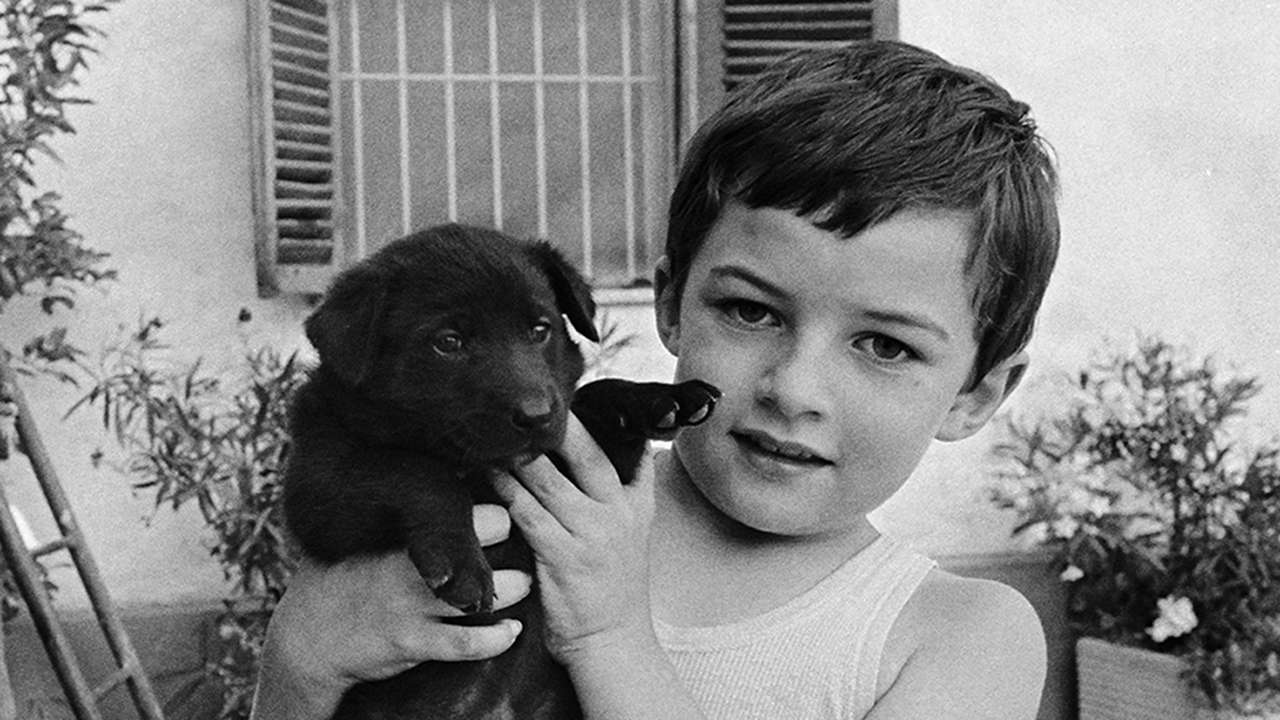 The image is in black and white. There is a child holding a puppy dog.