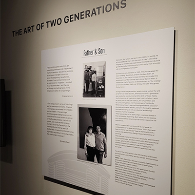 The wall has a title at the top: "The Art of Two Generations." Below this, there is a white panel with the title "Father and Son." The panel contains some text and two images of the duo.