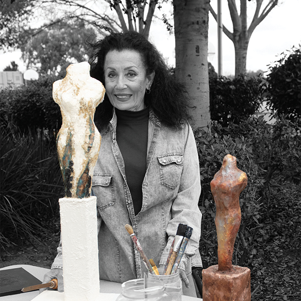 An image of the artist Tricia Grame in black and white, casually dressed, with two sculptures in color.