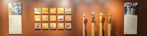 An image of a brown wall with a sequence of small paintings by Elena on the left and four sculptures by Tricia on the right. At the end of both sides, there is a bio of each artist.