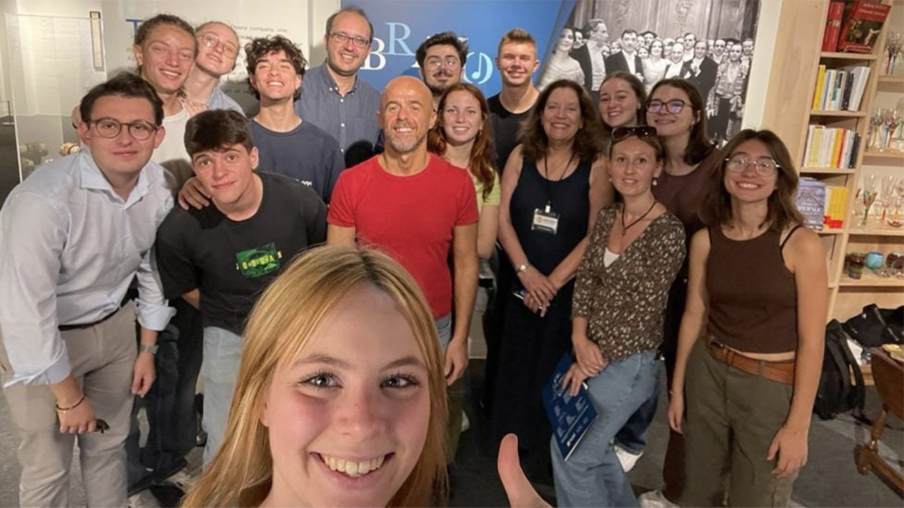 An image of a group of high school students posing for a selfie. Among them few adults and the director of the Museo. In the back on the wall the visual from our exhibit Bravo.