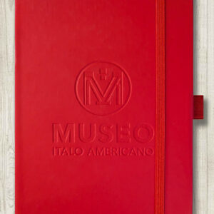 A red notebook featuring an embossed Museo logo, held closed by an elastic band.