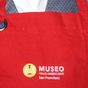 Image of a red apron featuring an embroidered Museo logo.