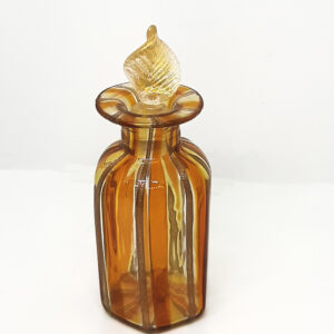 An orange and gold glass perfume bottle, with a golden leaf-shaped stopper.
