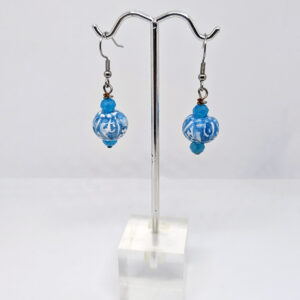 A pair of dangle earrings with a glass bead painted with sky blue swirling patterns, on silver hooks accented with small blue beads.