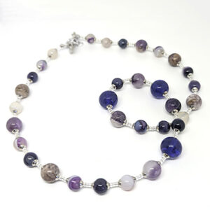 A string necklace with purple-hued glass beads with silver spacer beads.