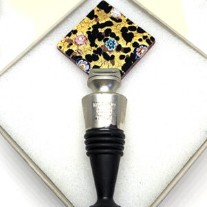 A square-shaped, glass wine stopper with a speckled dark brown on gold design, featuring a few small millefiore flowers.