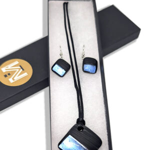 An earring and necklace set with matching square glass pendants featuring blue foil against a black background with matte black paint across half. The necklace's pendant is on a black cord, and earring's smaller pendants are on silver hooks.