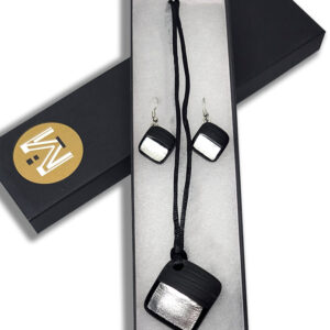 An earring and necklace set with matching square glass pendants featuring silver foil against a black background with matte black paint across half. The necklace's pendant is on a black cord, and earring's smaller pendants are on silver hooks.