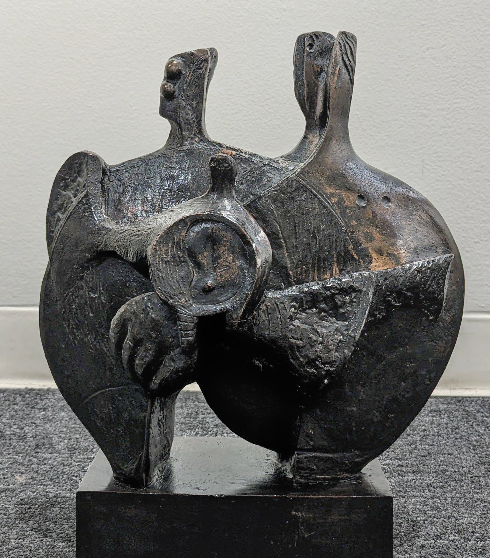 Bronze sculpture with two rounds forms representing parents. The forms are joined together at the sides and in the center of the sculpture there is a smaller form representing a child.