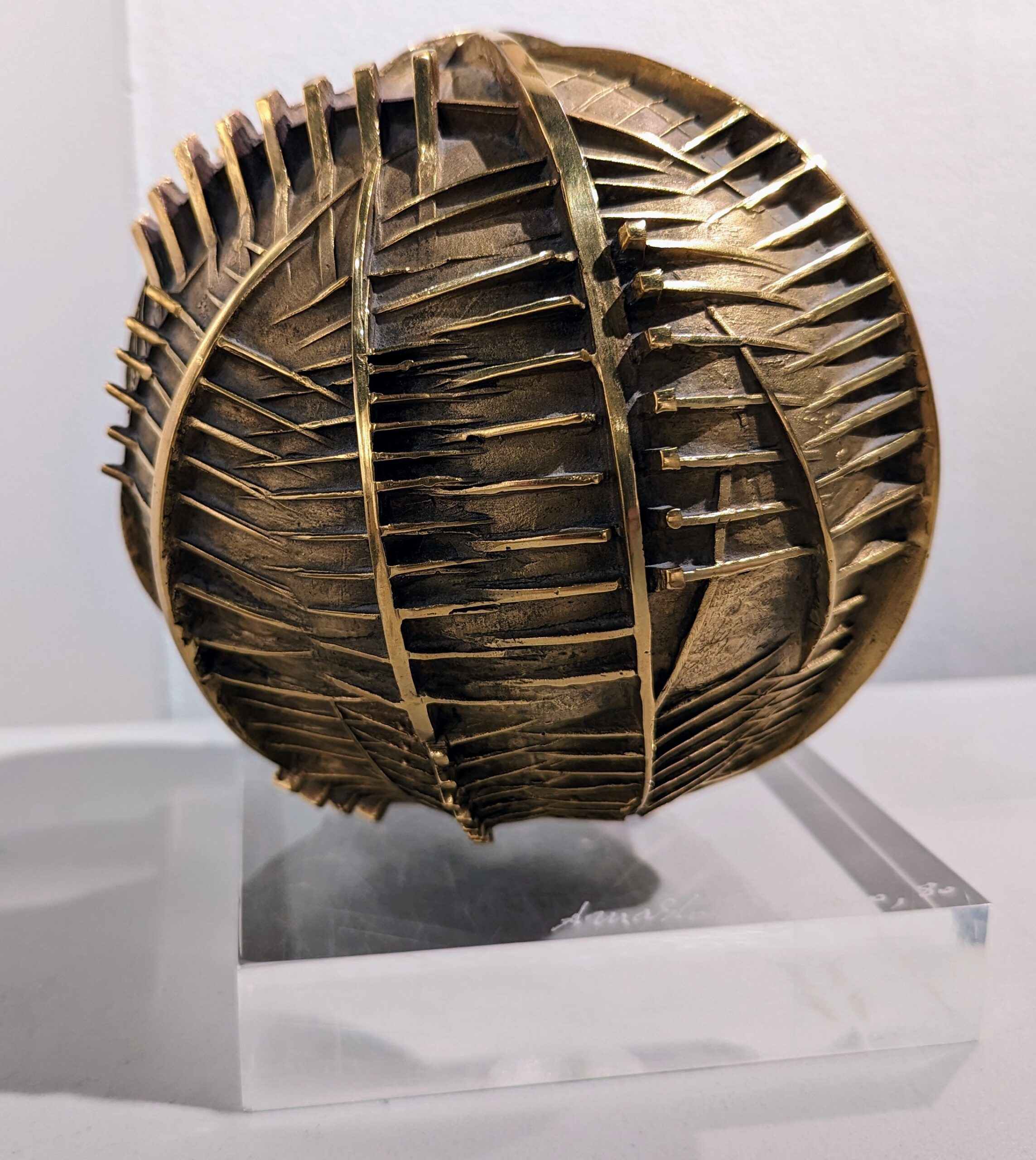 Golden bronze spherical sculpture with geometric lines weaving in and out of the sphere.