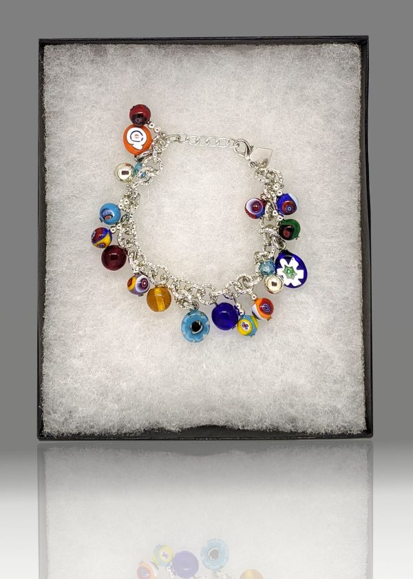 A charm bracelet is being crafted using the traditional millefiori (thousand-flowers) technique, where thin rods of glass (called murrine) are carefully arranged in a pattern and then heated until they fuse together. The bracelet is designed in bright colors reminiscent of carnevale.